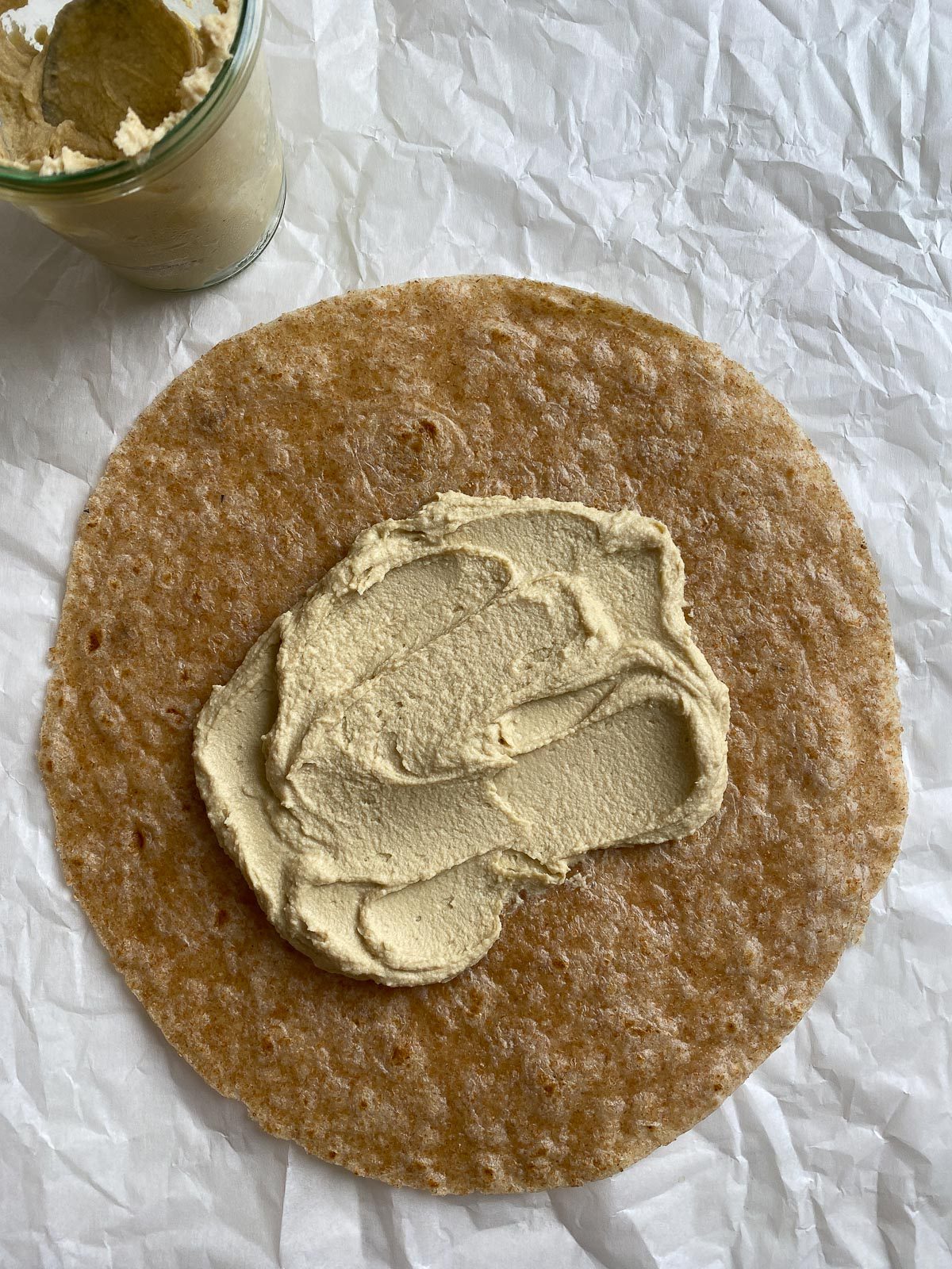process shot of hummus spread on tortilla against light surface