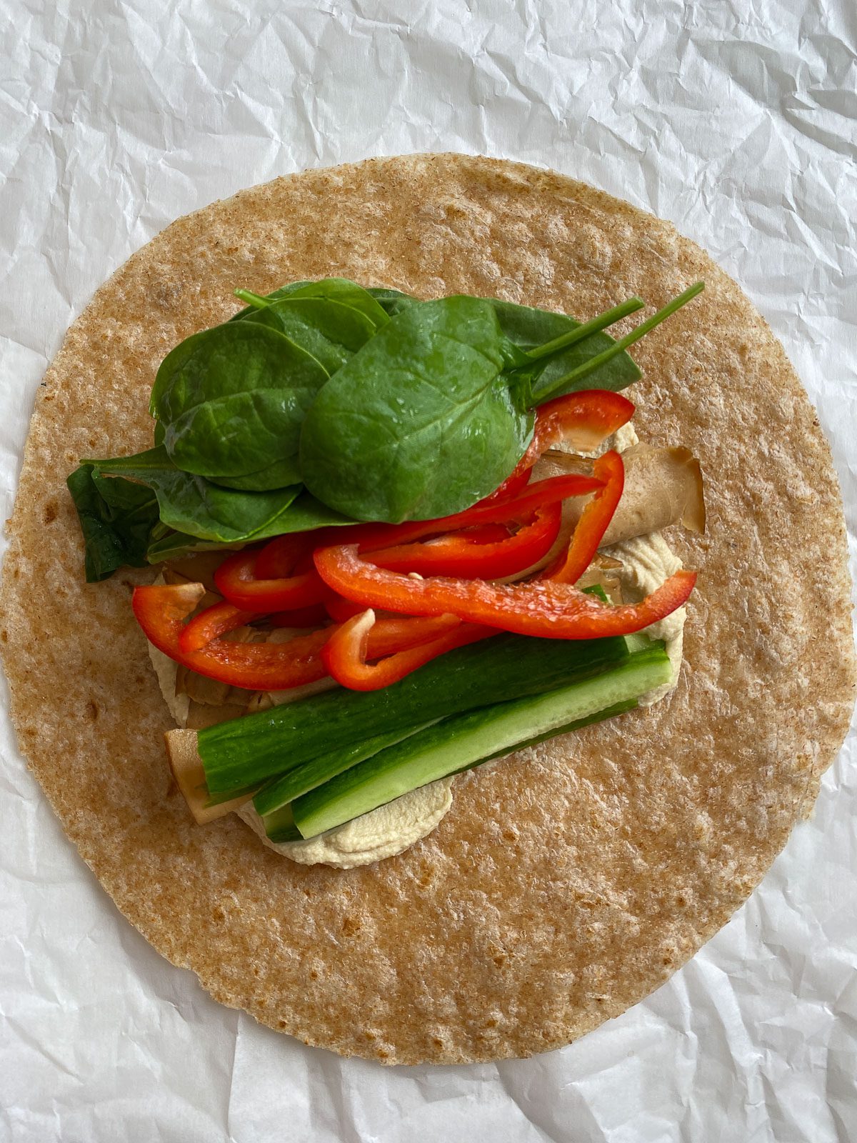 veggies added on top of hummus and tortilla against light surface