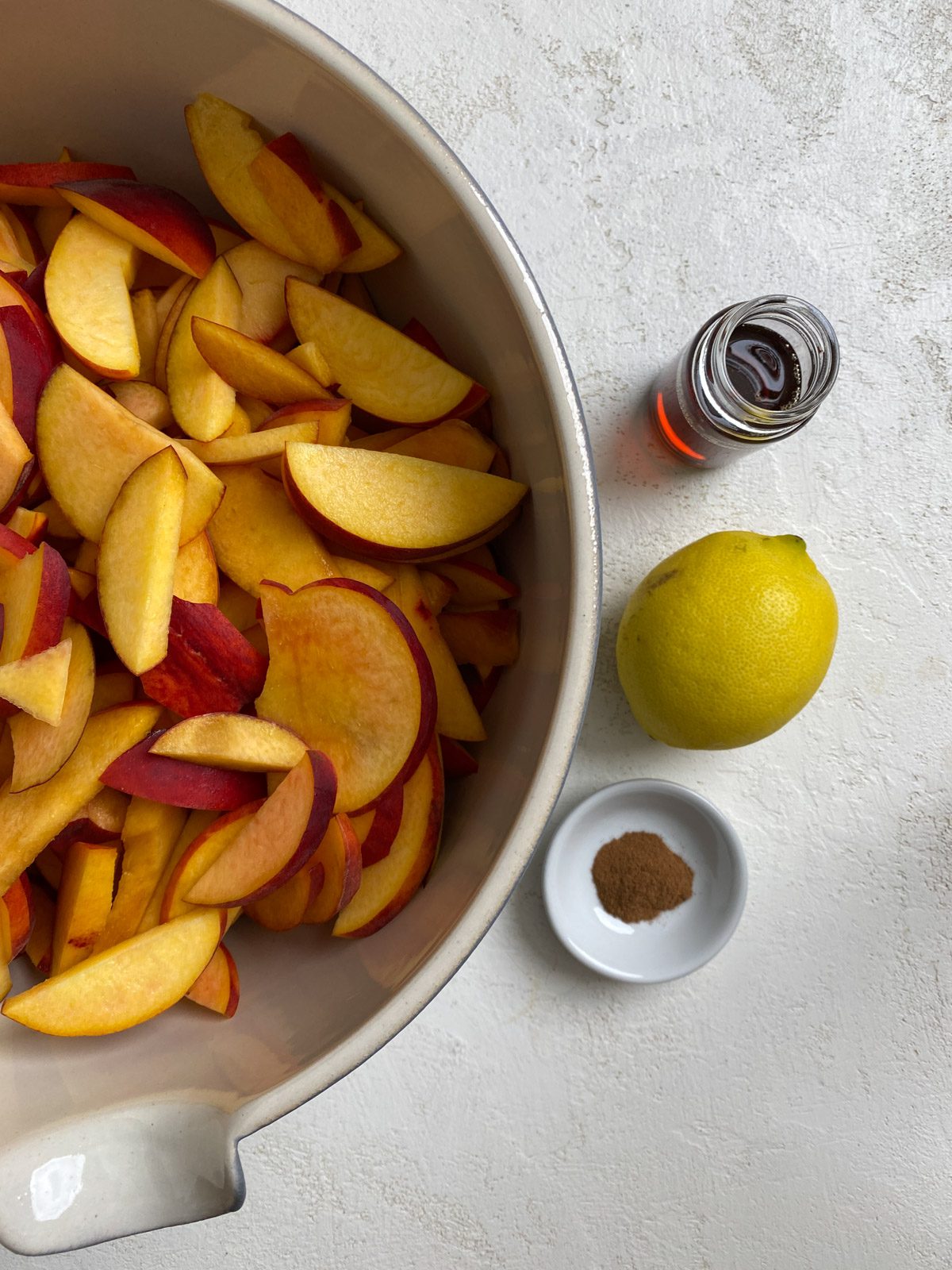 sliced peaches in a bowl alongside a bowl of ingredients against a light background