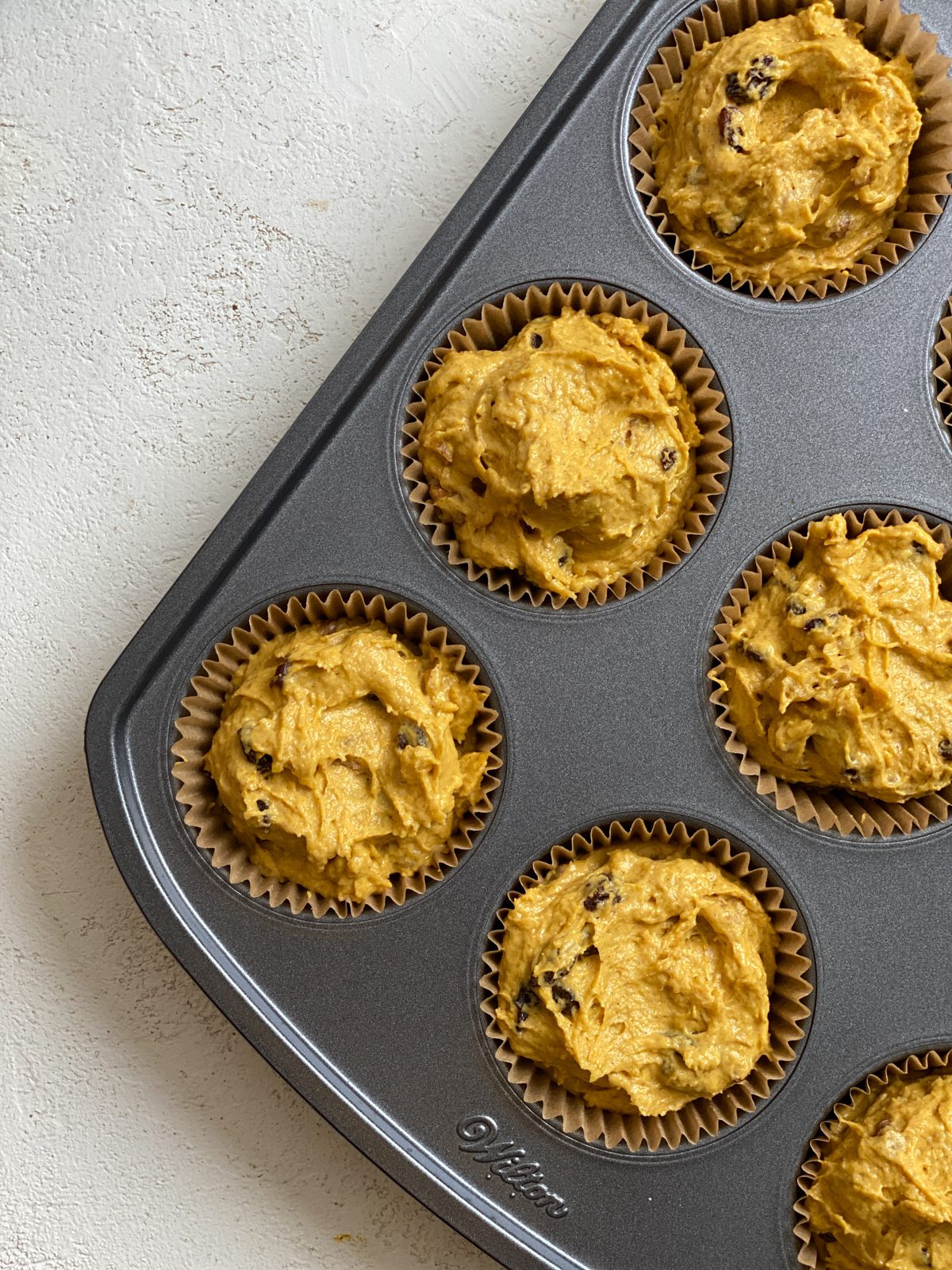 pre baked pumpkin muffins in a muffin tin against a white background