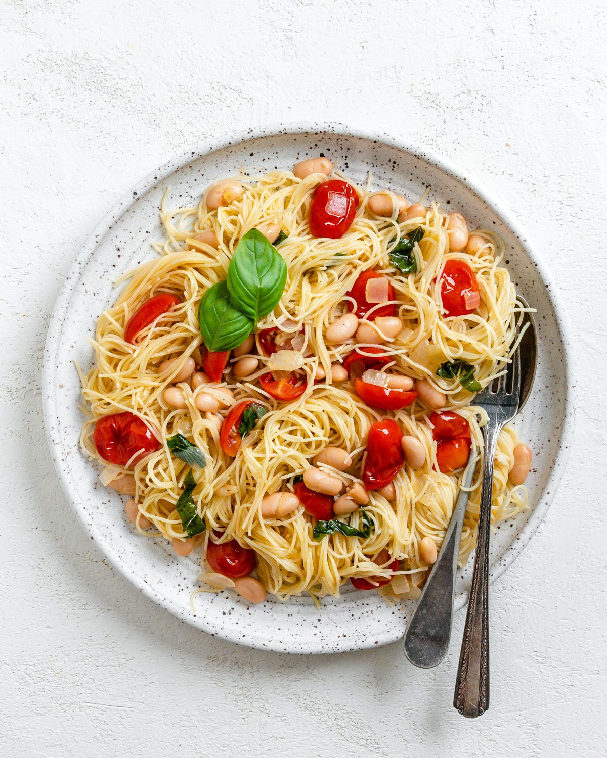 Completed Vegan Tomato Basil Angel Hair Pasta in a white plate against a light background.