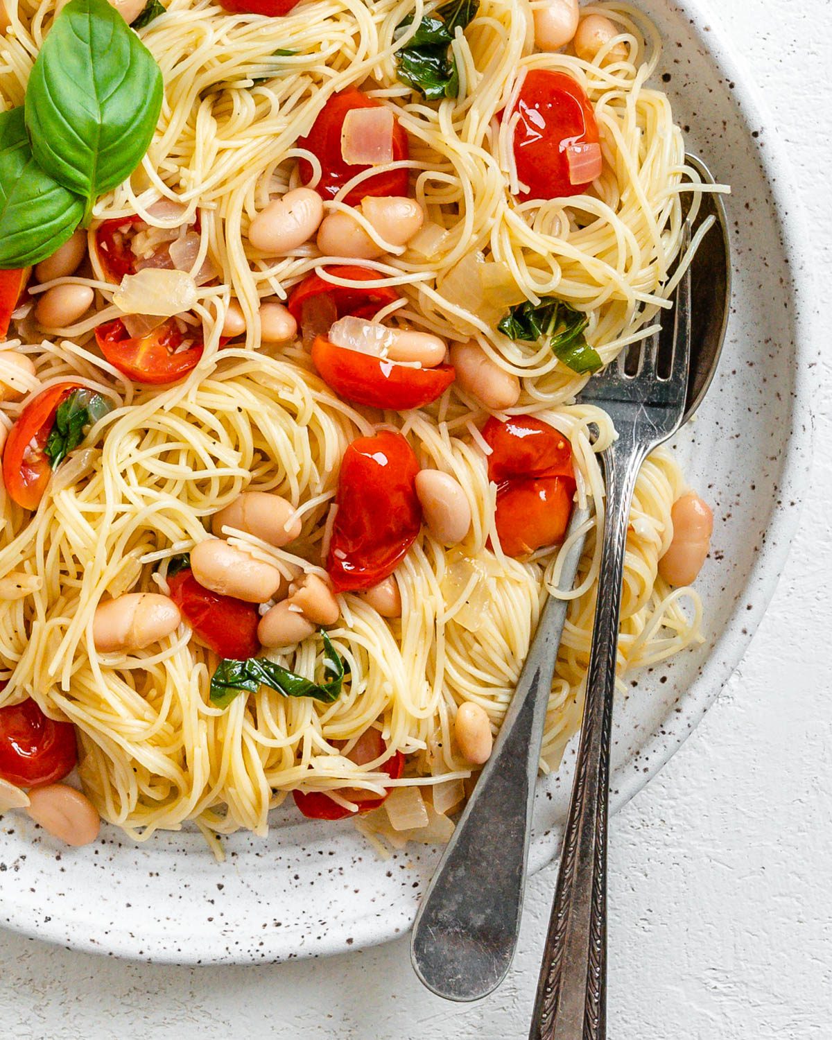 Completed Vegan Tomato Basil Angel Hair Pasta in a white plate against a light background.