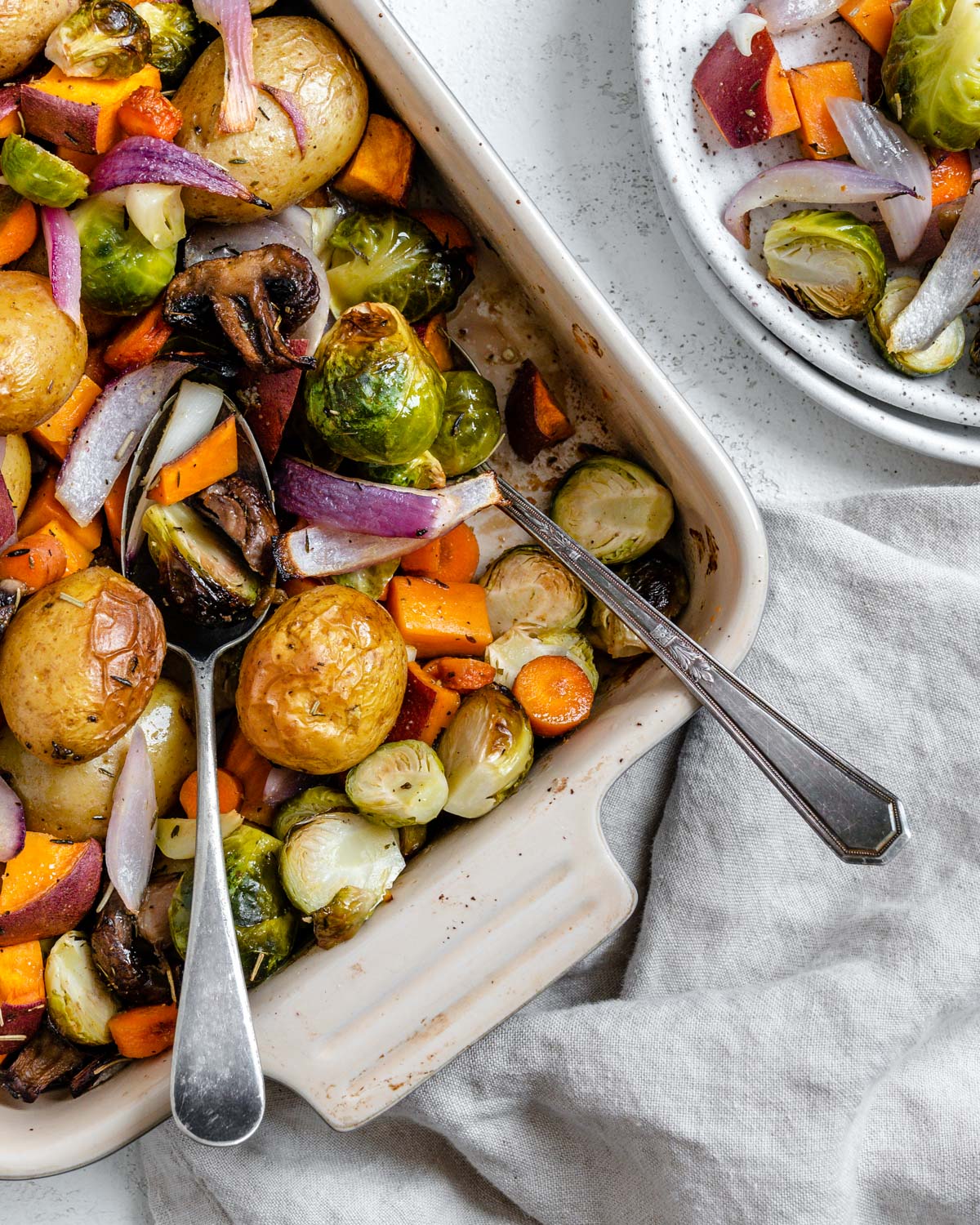 completed Roasted Vegetables in a baking dish alongside a bowl of veggies against a light surface