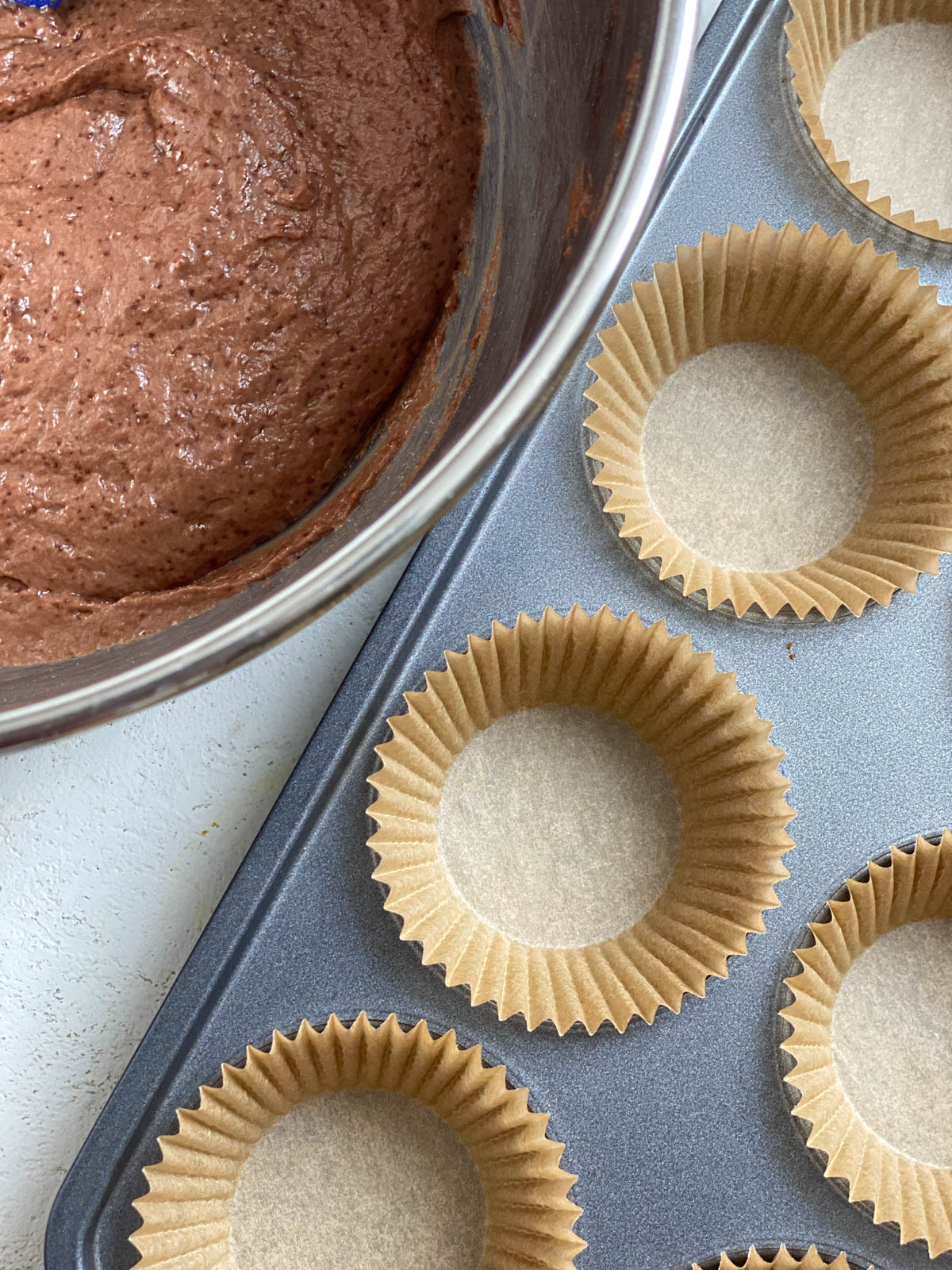process shot of bowl of batter alongside muffin tin prior to being poured into tin