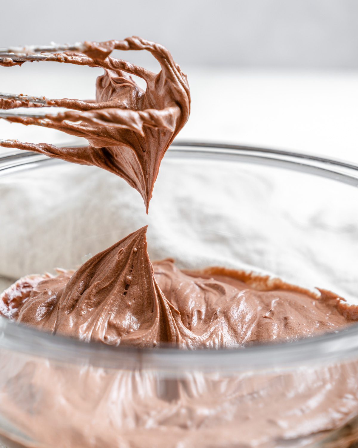 completed Vegan Chocolate Frosting in a bowl against a white background with a mixer on top