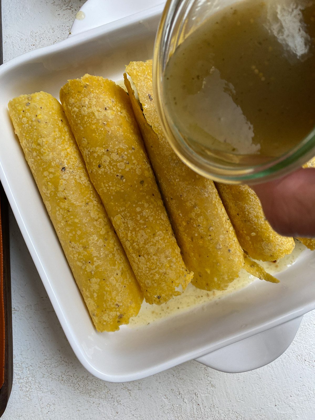 process shot of adding sauce to enchiladas in baking tray