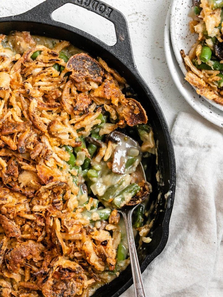 completed Dairy-Free Green Bean Casserole in a skillet with a portion plated on a white plate