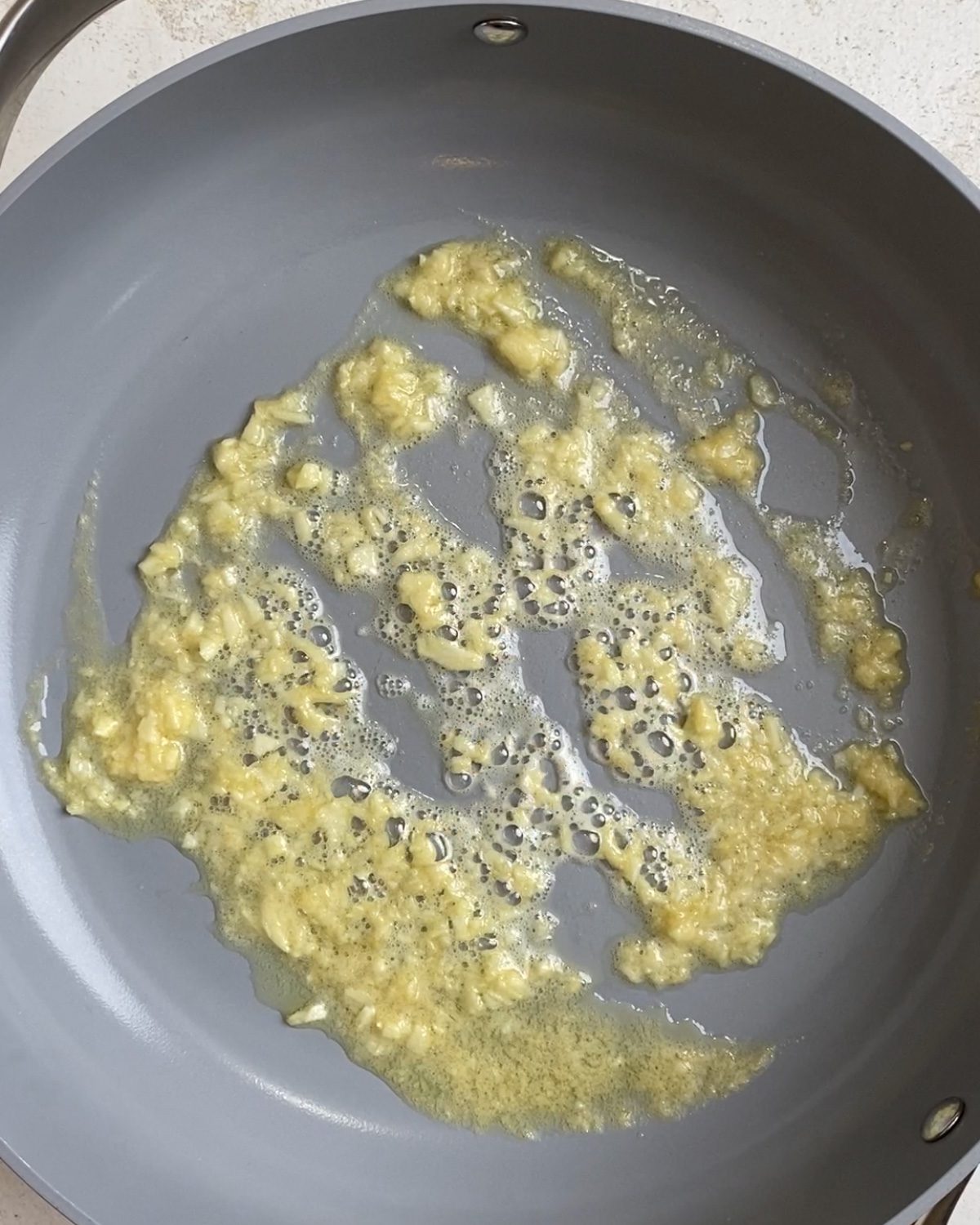 Process shot of butter and garlic cooking on a pan.