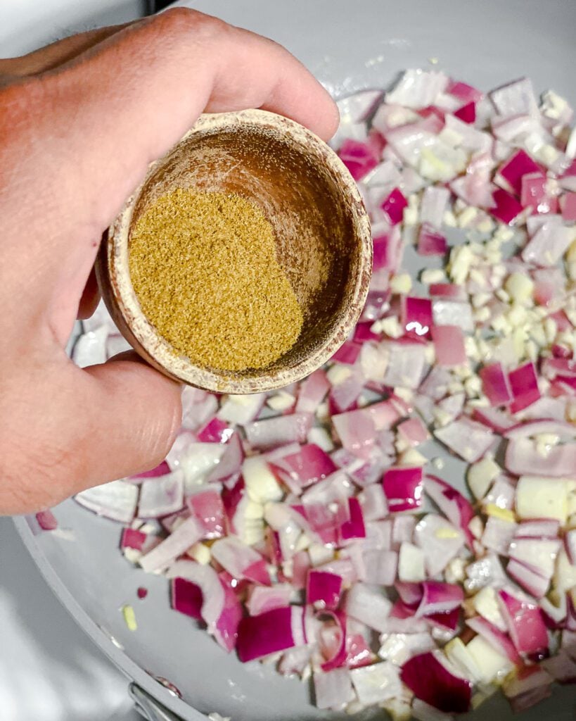 process shot of adding cumin to pan