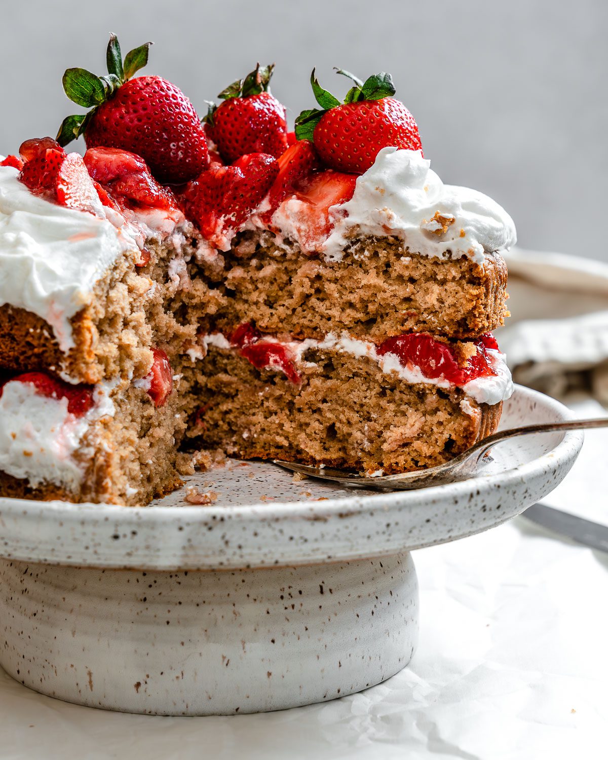 completed Vegan Strawberry Shortcake with a slice missing on a cake stand