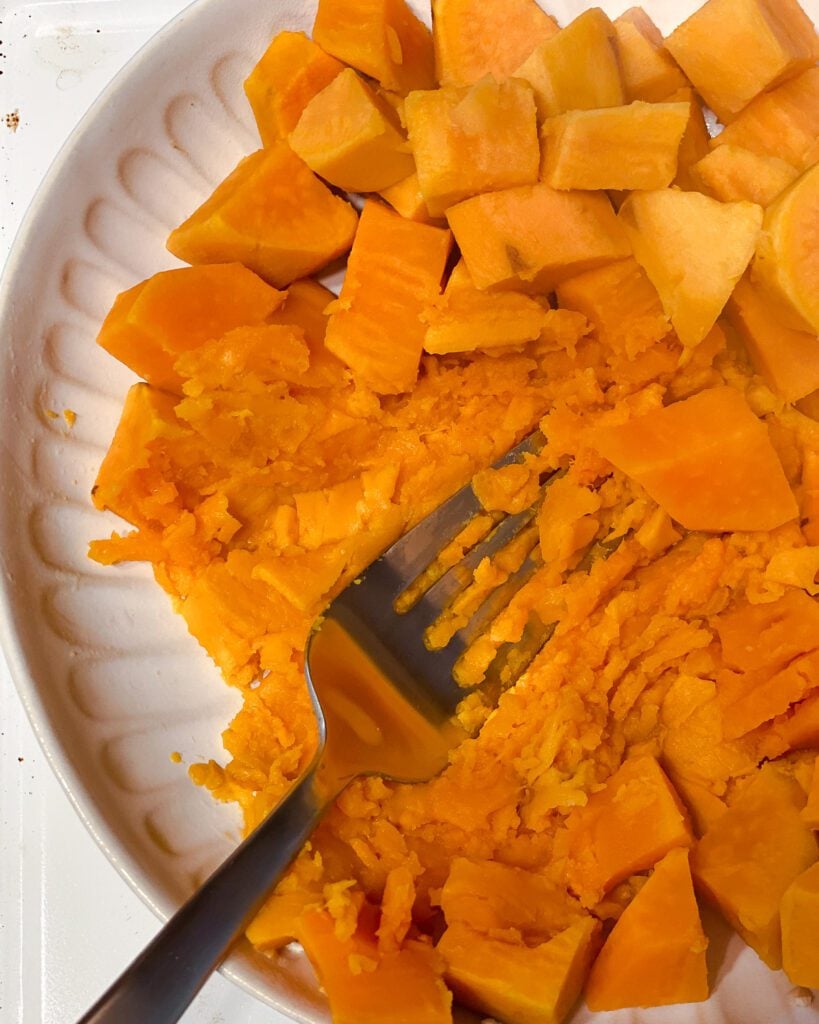 process shot of mashing sweet potatoes with fork