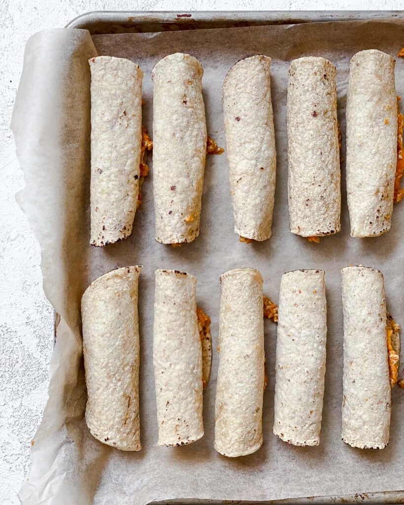 process shot showing several pre-baked taquitos on a baking dish