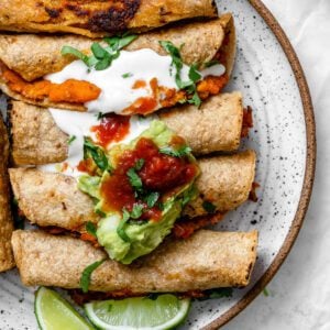 completed Vegan Taquitos against a white surface and topped with garnishes