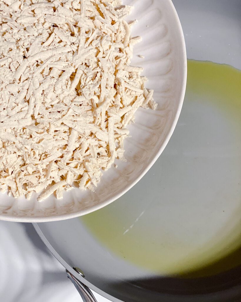 process shot of adding shredded tofu to pan