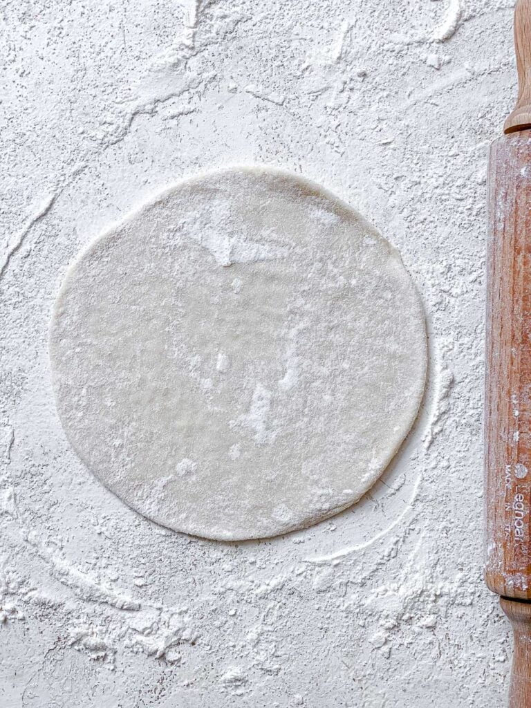 process shot of flattening dough on white floured surface