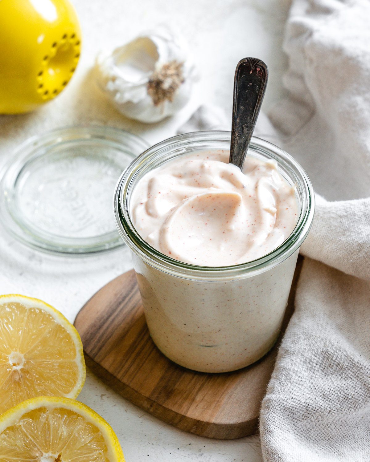 completed 5-Minute Vegan Garlic Aioli in a glass container with ingredients in the background