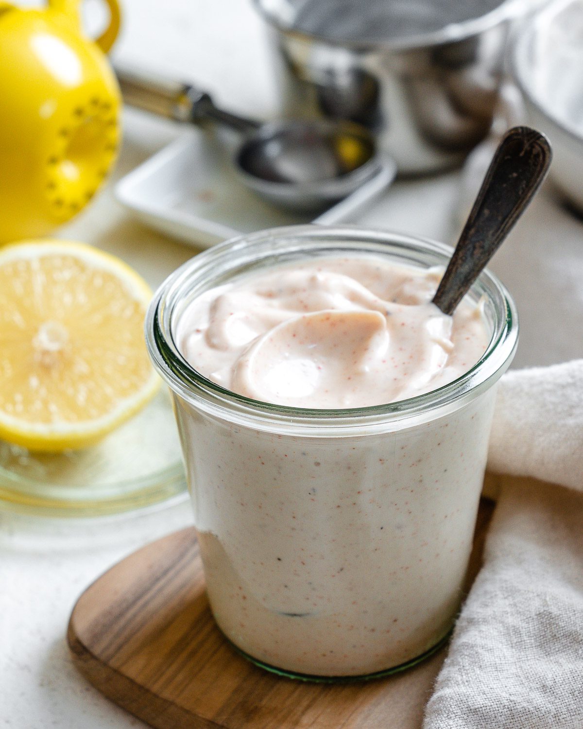 completed 5-Minute Vegan Garlic Aioli in a glass container with ingredients in the background