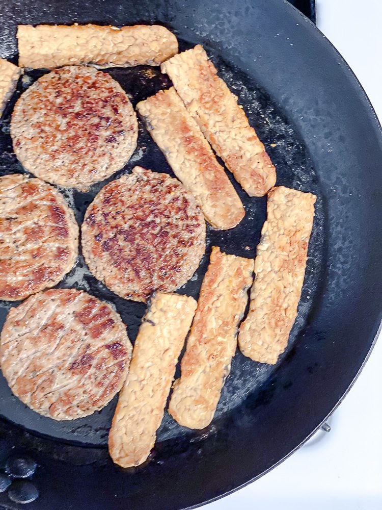 process shot of plant-based patties and tempeh cooking on pan