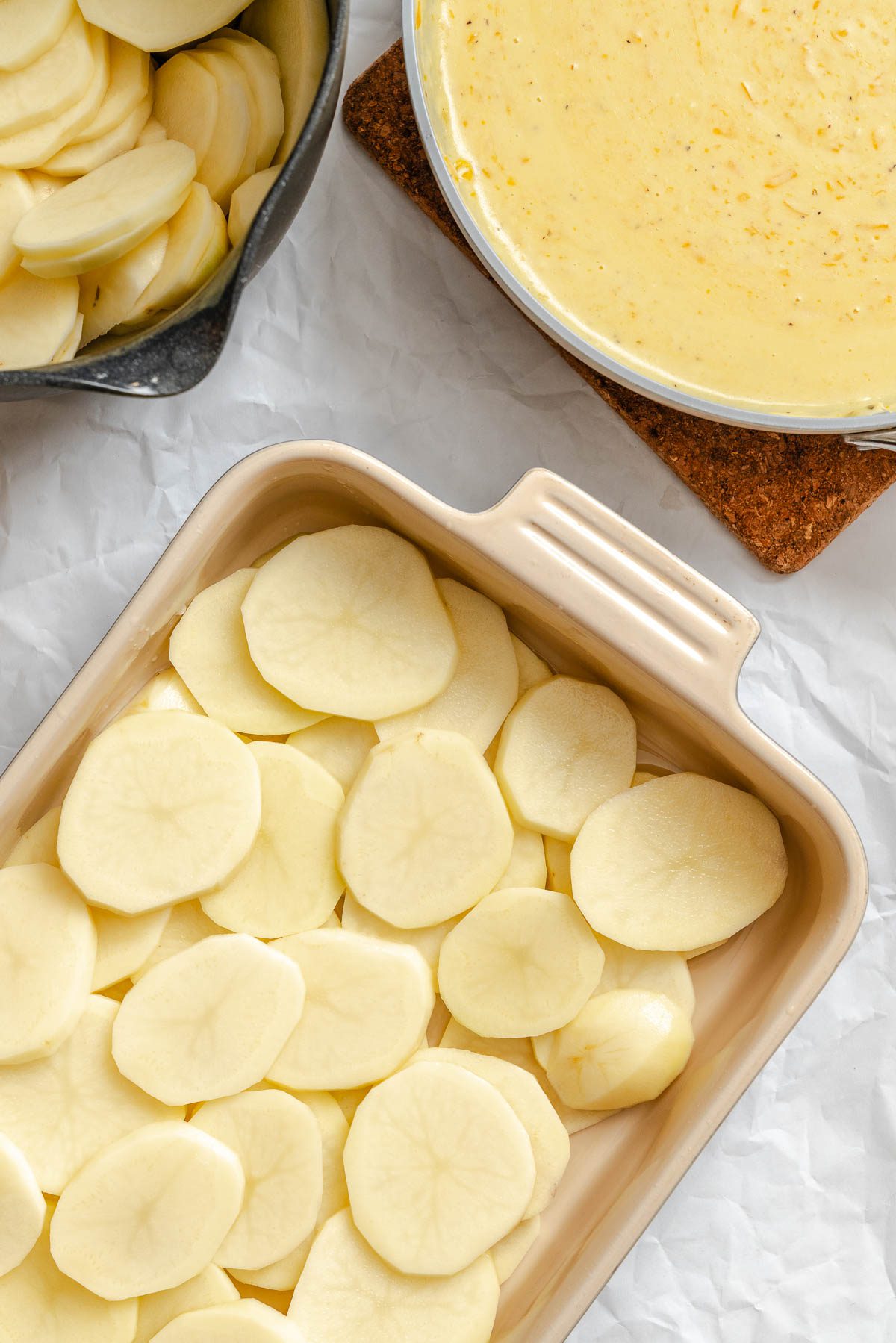 Process shot showing potatoes added to baking dish.